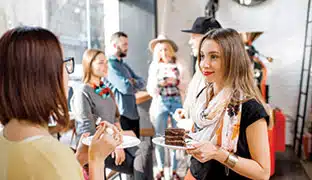 People standing having a conversation and eating cake