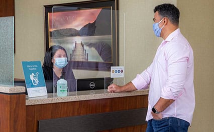 Man in a face mask talking to a woman at the reception desk, also in a face mask for safety.