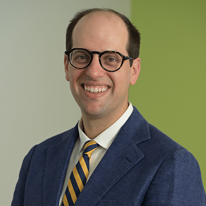 Erich Russel, DO radiologist in Maine guy smiling with black framed glasses in blue suit jacket and yellow striped tie