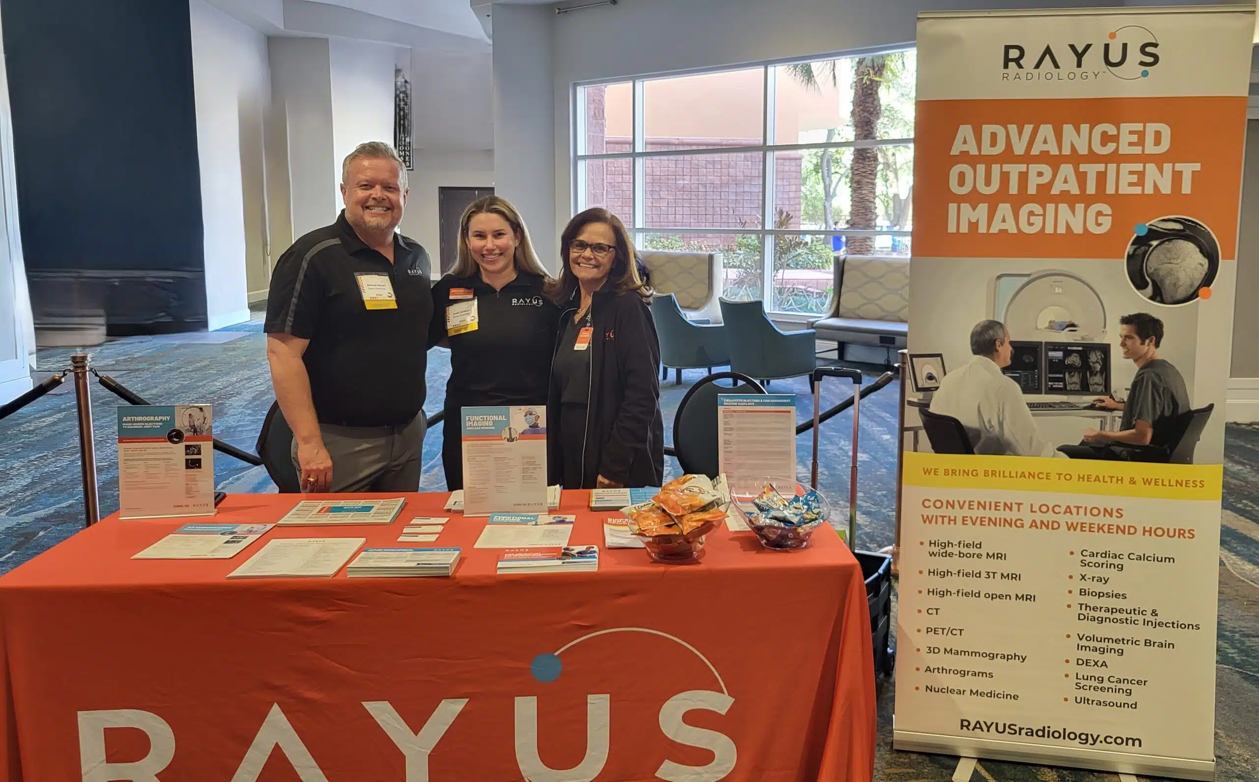 1 male and 2 females behind a rayus radiology booth